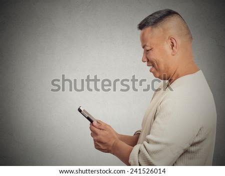 Closeup side profile portrait happy cheerful middle aged man excited by what he sees on his cell phone isolated grey wall background copy space. Positive human emotion face expression feeling reaction
