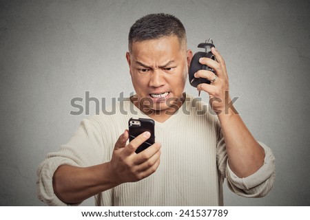 Headshot unhappy angry middle aged man with alarm clock looking at smart phone with frustrated face expression late for meeting isolated grey background. Human expression emotion feeling reaction