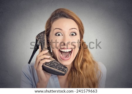 Headshot young happy woman looking excited, holding an high heeled shoe in her hand as a phone isolated on grey wall background. human face expression emotion feelings