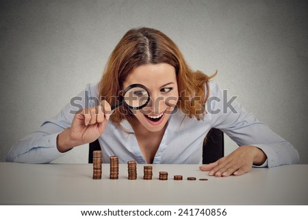 Closeup portrait excited greedy business woman wall street executive looking at growing stack of coins through magnifying glass isolated grey wall office background. Human face expression. Economy
