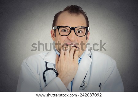 Closeup portrait young insecure, crazy male doctor uncertain psychiatrist with glasses looking funny, scared, craving anxious isolated grey background. Human face expression emotion feeling perception
