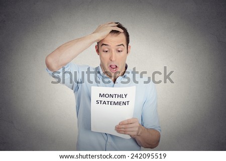 Closeup portrait sad shocked funny looking young man disgusted at his corporate monthly statement isolated grey background. Negative human emotion facial expression feeling. Financial crisis, bad news