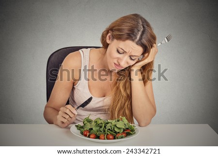 sad displeased young woman eating salad isolated grey wall background. Negative human face expression emotion.