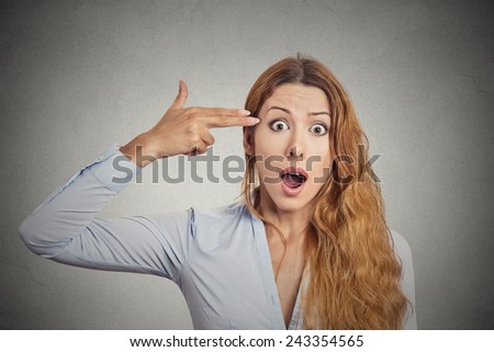 Portrait stressed young woman with hand finger gun gesture shocked wide open mouth isolated on grey wall background. Negative human emotions face expression feelings life perception