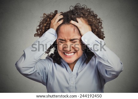 Frustrated stressed young woman. Headshot unhappy overwhelmed girl having headache bad day pulling her hair out isolated on grey wall background. Negative emotion face expression feelings perception 