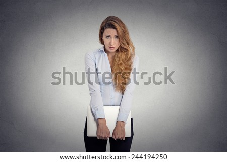 Lack of confidence. Insecure worried young woman holding laptop feels awkward isolated grey wall background. Human face expression emotion body language life perception