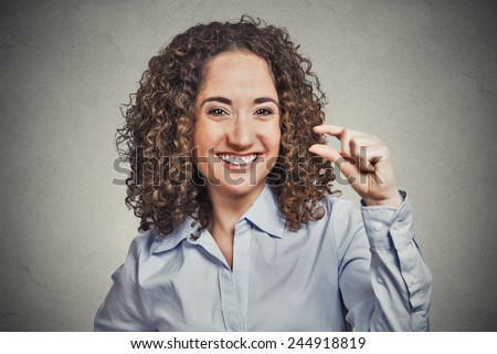 Closeup portrait, funny young curly brown hair woman showing small amount gesture with hand fingers isolated grey background. Human emotion facial expression feelings, body language, signs, symbols