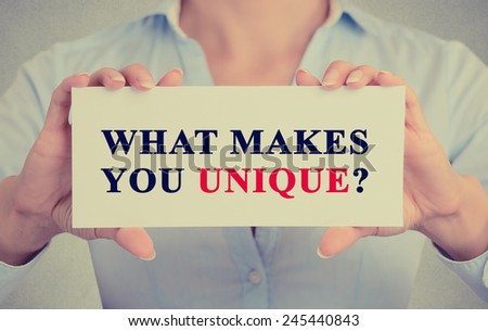 Closeup retro image businesswoman female executive hands holding white sign or card with message text phrase what Makes You Unique? isolated on gray office wall background