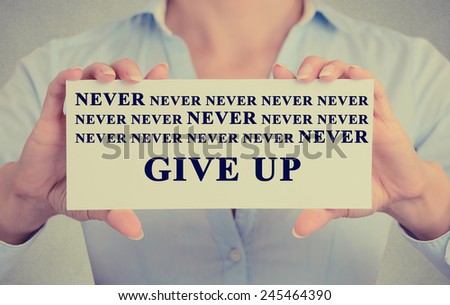 Retro Instagram vintage style image of businesswoman hands holding white card with never give up sign message isolated on grey wall office background.