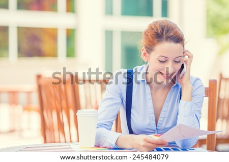 Portrait young professional woman talking on mobile phone reviewing documents papers outside corporate office isolated city building background. Positive face expression emotion, life success concept