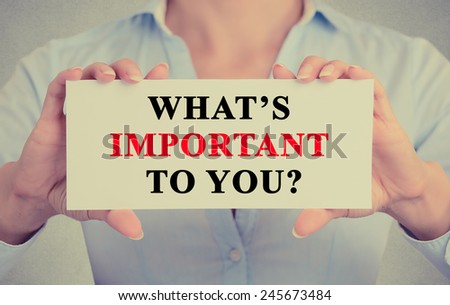 Businesswoman hands holding white card sign with What is important to you ? question text message isolated on grey wall office background. Retro instagram style image