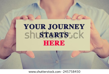 Closeup businesswoman hands holding white card sign with Your Journey Starts Here text message isolated on grey wall office background. Retro instagram style image