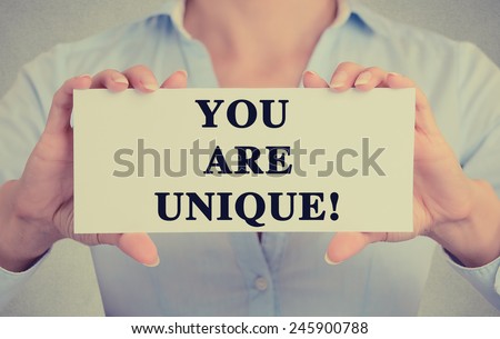 Closeup businesswoman hands holding white card sign with you are unique text message isolated on grey wall office background. Retro instagram style image