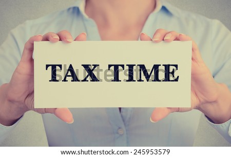 Closeup businesswoman hands holding white card sign with tax time text message isolated on grey wall office background. Retro instagram style image