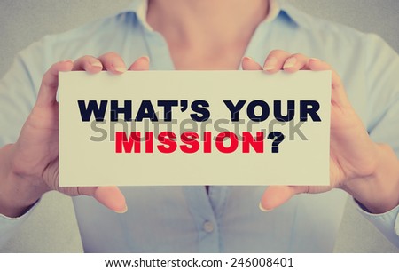 Closeup businesswoman hands holding white card sign with what\'s your mission question text message isolated on grey wall office background. Retro instagram style image