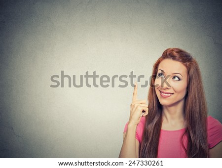 Portrait happy beautiful woman thinking looking up pointing with finger at blank copy space isolated grey wall background. Positive human face expressions, emotions, feelings body language, perception