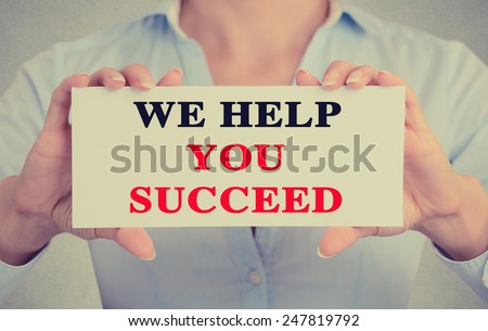 Businesswoman hands holding white card sign with we help you succeed text message isolated on grey wall office background. Retro instagram style image