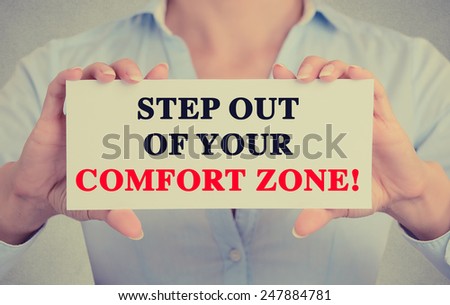 Businesswoman hands holding white card sign with step out of your comfort zone text message isolated on grey wall office background. Retro instagram style image