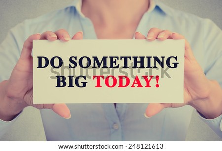 Businesswoman hands holding white card sign with do something big today text message isolated on grey wall office background. Retro instagram style image