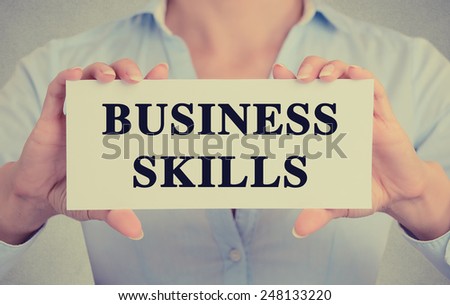 Closeup businesswoman hands holding white card sign with business skills text message isolated on grey wall office background. Retro instagram style image