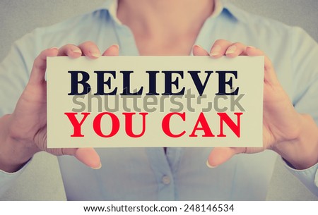 Closeup businesswoman hands holding white card sign with believe you can text message isolated on grey wall office background. Retro instagram style image