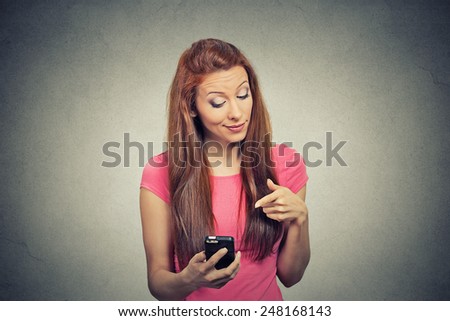 Portrait young angry woman unhappy, annoyed by something, someone on her cell phone while texting, receiving bad sms text message isolated grey wall background. Human face expression emotion reaction