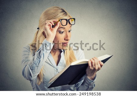 Closeup portrait headshot young woman wide opened eyes looking at book page shocked surprised by twists turn of story isolated grey wall background. Human emotion facial expression feeling reaction