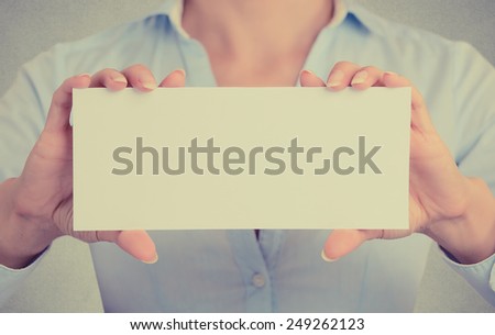Closeup businesswoman hands holding white card sign with blank copy space for advertisement text message isolated on grey wall office background. Cropped retro instagram style image