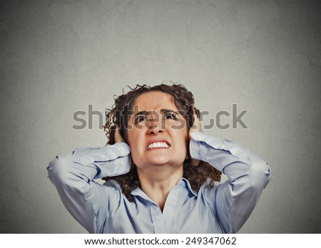 Closeup portrait young angry unhappy stressed woman covering her ears looking up stop making loud noise it\'s giving me headache isolated grey wall background. Negative emotion face expression feeling