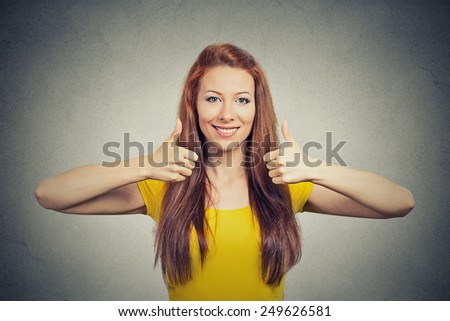 Happy smiling woman with thumbs up gesture isolated grey wall background. Positive emotion face expression sign symbol body language