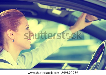 Happy young woman driver looking adjusting rear view car mirror, making sure line is free visibility is good before making turn. Human facial expressions, emotions. Safe trip, journey driving concept