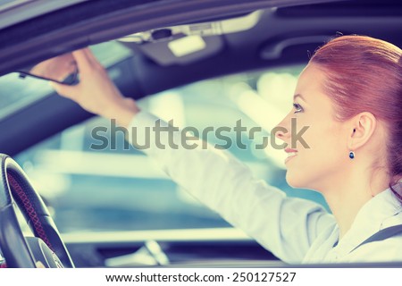 Happy young woman driver looking adjusting rear view car mirror, making sure line is free visibility is good before making turn. Human facial expressions, emotions. Safe trip, journey driving concept