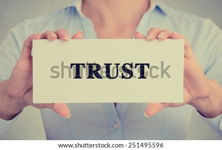 Closeup businesswoman hands holding white card sign with trust text message isolated on grey wall office background. Retro instagram style image