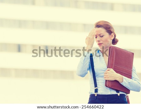 Portrait stressed worried unhappy young woman corporate employee having headache migraine  isolated outdoors on corporate office windows building background. Negative human emotions face expression