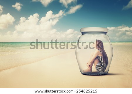 young woman sitting in a glass jar on a beach looking at the ocean view. Loneliness outlier person. After storm survivor message to future generation concept