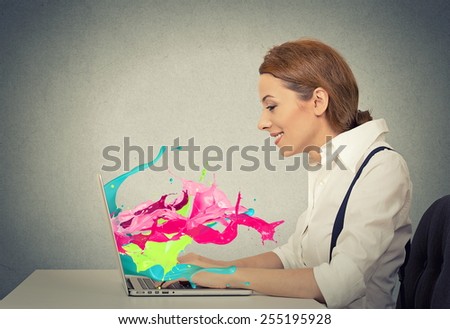 Side view profile attractive happy young business woman working on laptop computer colorful splashes coming out of screen liquid effect isolated grey wall background. Positive face expression vision