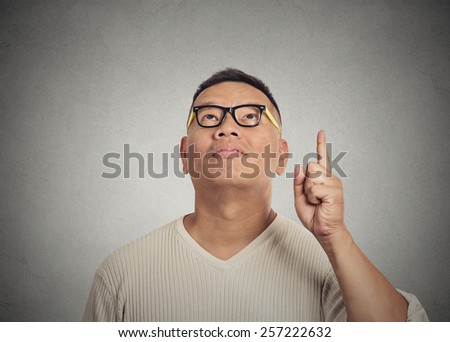 Portrait young man has an idea, pointing with finger up isolated on grey wall background. Excited guy with solution for a problem. Human face expression body language, life perception creativity