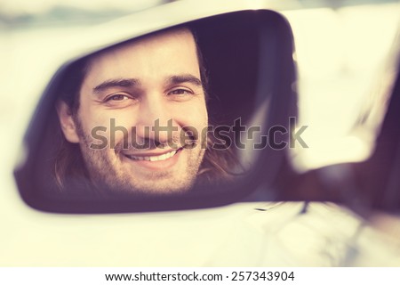 Happy young man driver looking in car side view mirror, making sure line is free before making a turn. Positive human face expression emotions. Safe trip journey driving concept