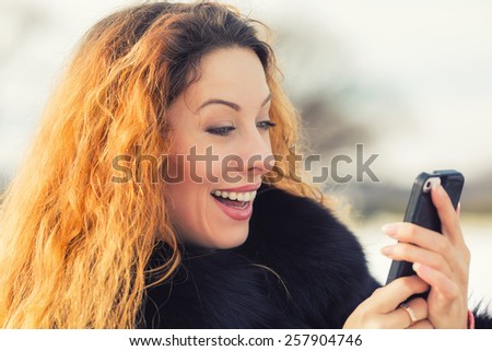 Closeup portrait, happy, cheerful, girl, excited by what she sees on cell phone, isolated park city street background. Facial expression, reaction. Beautiful woman sending text message from her mobile