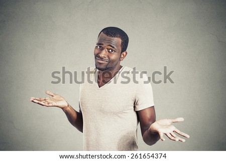 Young man shrugging shoulders who cares so what I don\'t know gesture isolated on grey wall background. Body language