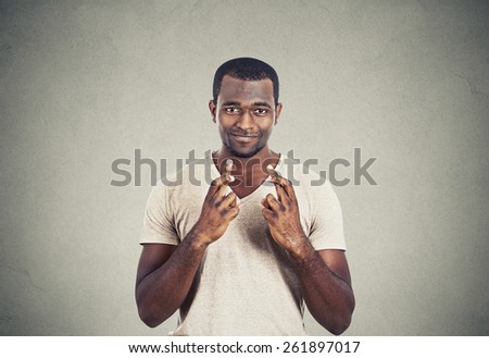 Young hopeful man crossing fingers isolated on grey wall background. Human face expression
