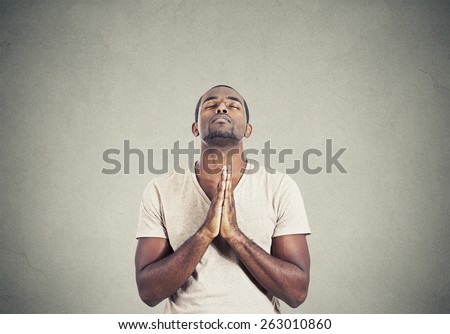 Closeup portrait young man praying hands clasped hoping for best asking for forgiveness or miracle isolated gray wall background. Human emotion facial expression feeling