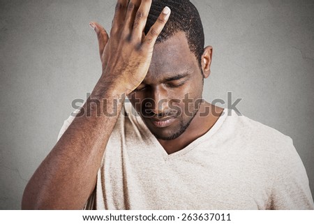 Closeup headshot very sad depressed, stressed, alone, disappointed gloomy young man head on hands having suicidal thoughts isolated grey wall background. Human emotion facial expression reaction
