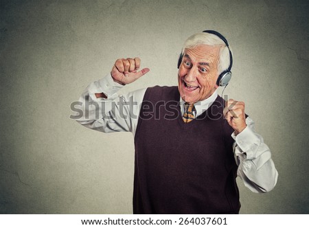 Closeup portrait elderly man, senior retired guy with headphones listening to the radio, enjoying music and his life isolated on gray wall background. Positive human emotions, face expression