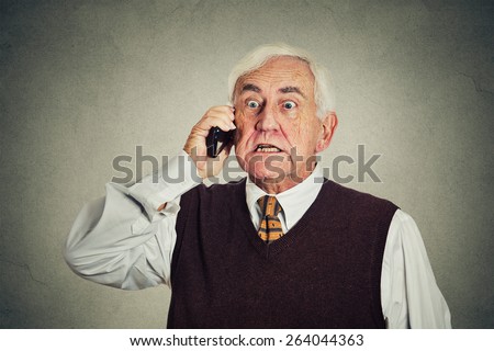 Angry senior man talking on mobile phone isolated on gray wall background. negative emotions