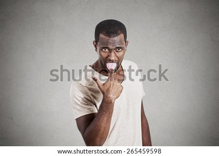 Young angry, unhappy man with finger in mouth something sucks gesture isolated on gray background. Negative facial emotions, expressions, feelings