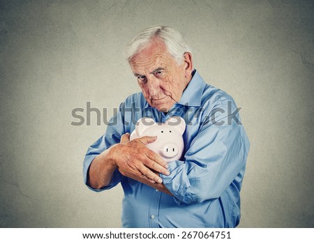 Senior man holding piggy bank isolated on gray wall background. Financial security planning concept