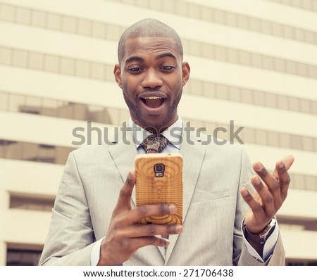 Closeup portrait surprised handsome young man looking at phone seeing unexpected news photos email isolated outside city building background. Human emotion, reaction, facial expression