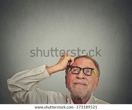 Closeup headshot undecided senior man with glasses scratching head thinking looking up isolated gray wall background with copy space. Human face expression emotion perception