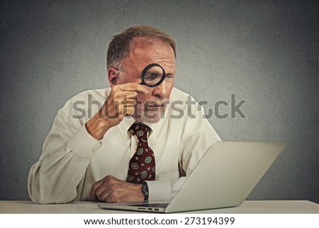 Curious. Business man working on computer looking through magnifying glass at laptop screen isolated gray wall background. Human face expression. Security safety social media concept